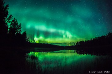 Groen noorderlicht reflecterend in een meer in centraal Finland.